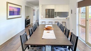Un comedor amplio con una larga mesa de madera, sillas tapizadas negras y una cocina moderna al fondo.