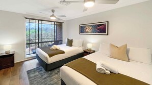 Habitación de hotel con dos camas, ventilador de techo, ventana grande con vistas y una obra de arte enmarcada en la pared.