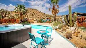 A pool area with a hot tub, two chairs, and a table.