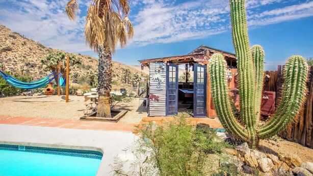 A desert landscape with a pool, a wooden structure, and large cacti.