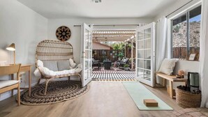 A cozy living room with a wicker chair, a wooden bench, and a dining area with outdoor seating.