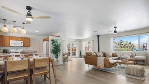 A spacious living area with a large window, a dining area with wooden furniture, and a kitchen with modern appliances.