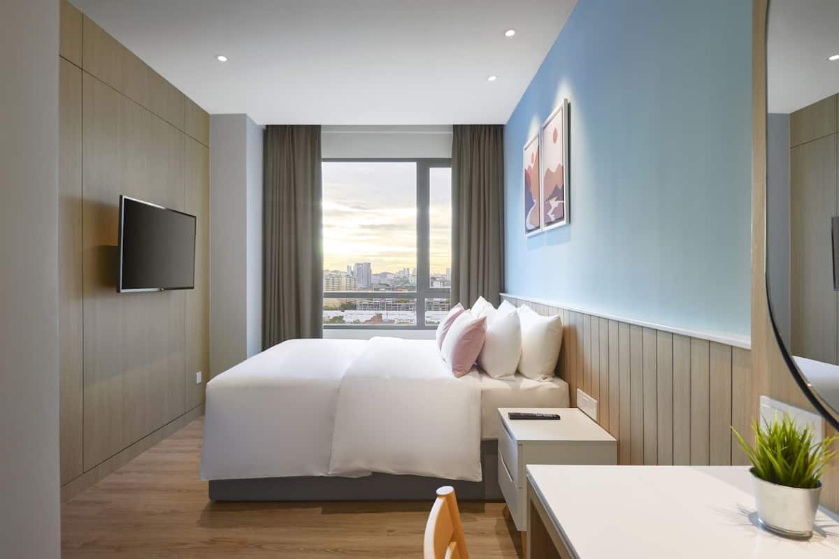A modern hotel room with a large bed, a desk, a TV, and a city view.