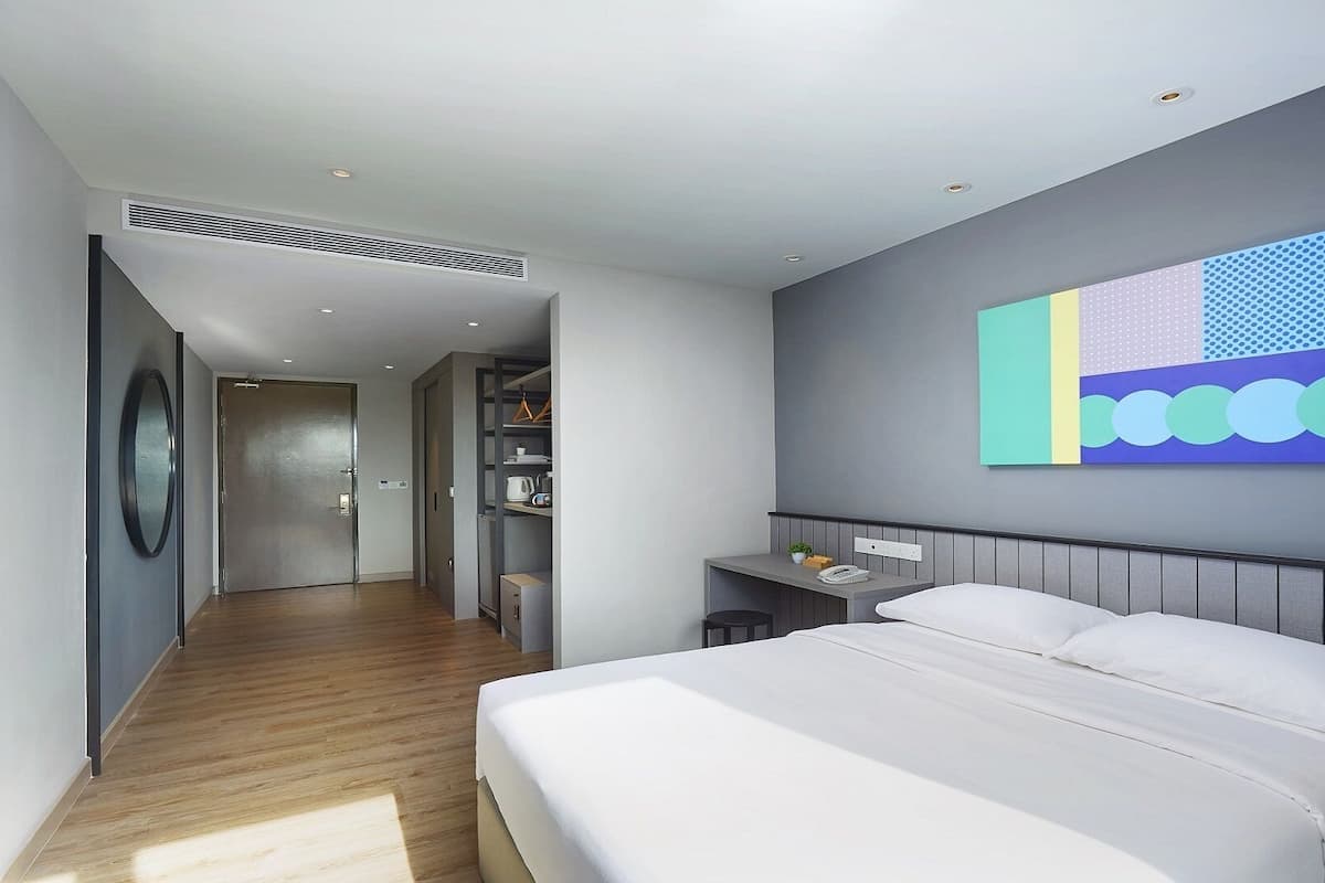 A modern hotel room with a large bed, a desk, and a colorful abstract painting on the wall.