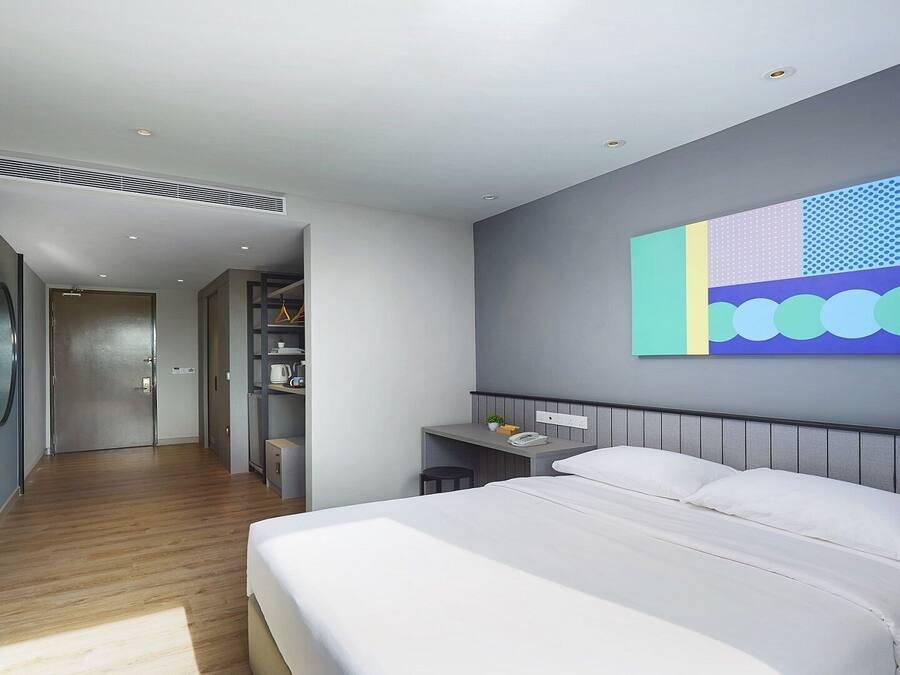A modern hotel room with a large bed, a desk, and a colorful abstract painting on the wall.