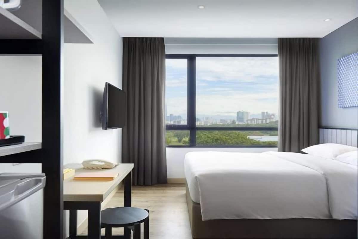 A modern hotel room with a large window, a bed, a desk, and a television.