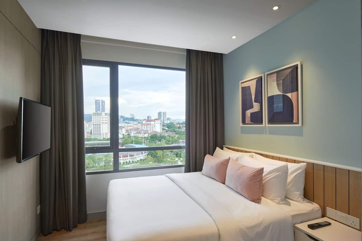 A hotel room with a large bed, a TV mounted on the wall, and a view of the cityscape through a large window.