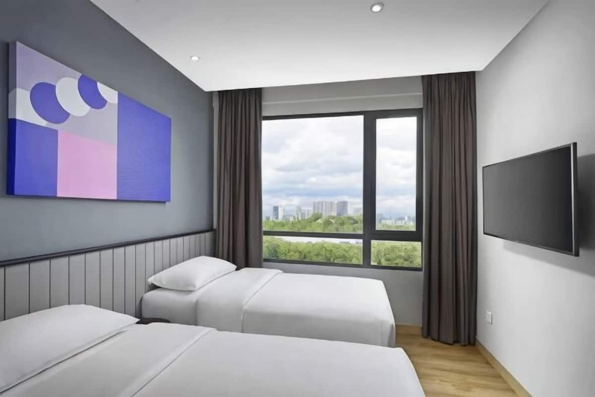 A hotel room with two beds, a large window with a city view, a flat-screen TV, and a modern abstract painting on the wall.