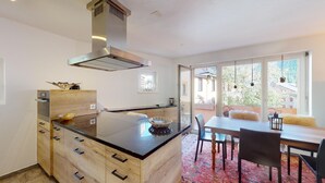 A modern kitchen with a central island, wooden cabinetry, and a stainless steel range hood. - 3½ room apartment, on the second floor, with lift. (Samedan)