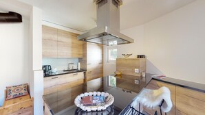 A modern kitchen with wooden cabinets, a glass backsplash, and a central island with a basket of magazines. - 3½ room apartment, on the second floor, with lift. (Samedan)