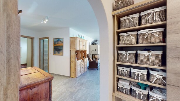 A hallway with a wooden cabinet, wicker baskets, and a painting on the wall. - 3½ room apartment, on the second floor, with lift. (Samedan)