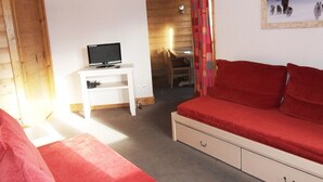 Una habitación con un sofá rojo, un televisor sobre un estante blanco y un techo de madera.