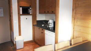 Una cocina compacta con armarios de madera, un microondas, una cafetera y un refrigerador pequeño.