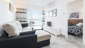 A modern living room with a sofa, a TV, a bed, and a balcony with curtains.