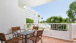 A balcony with wicker chairs and a table, overlooking a pool and greenery.