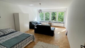 Ein modernes Schlafzimmer mit Bett, Sofa, Kleiderschrank und einem großen Fenster für natürliches Licht.