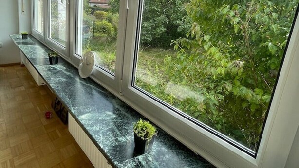 Ein Zimmer mit einem großen Fenster, das auf einen Garten und ein Haus blickt.