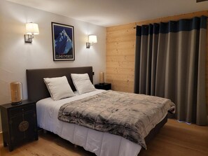 A bedroom with a bed, two bedside tables, a wall-mounted lamp, a poster, and a wooden wall panel.