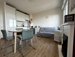 A compact living space with a kitchenette, a dining area with a table and chairs, a grey sofa, and a small heater.