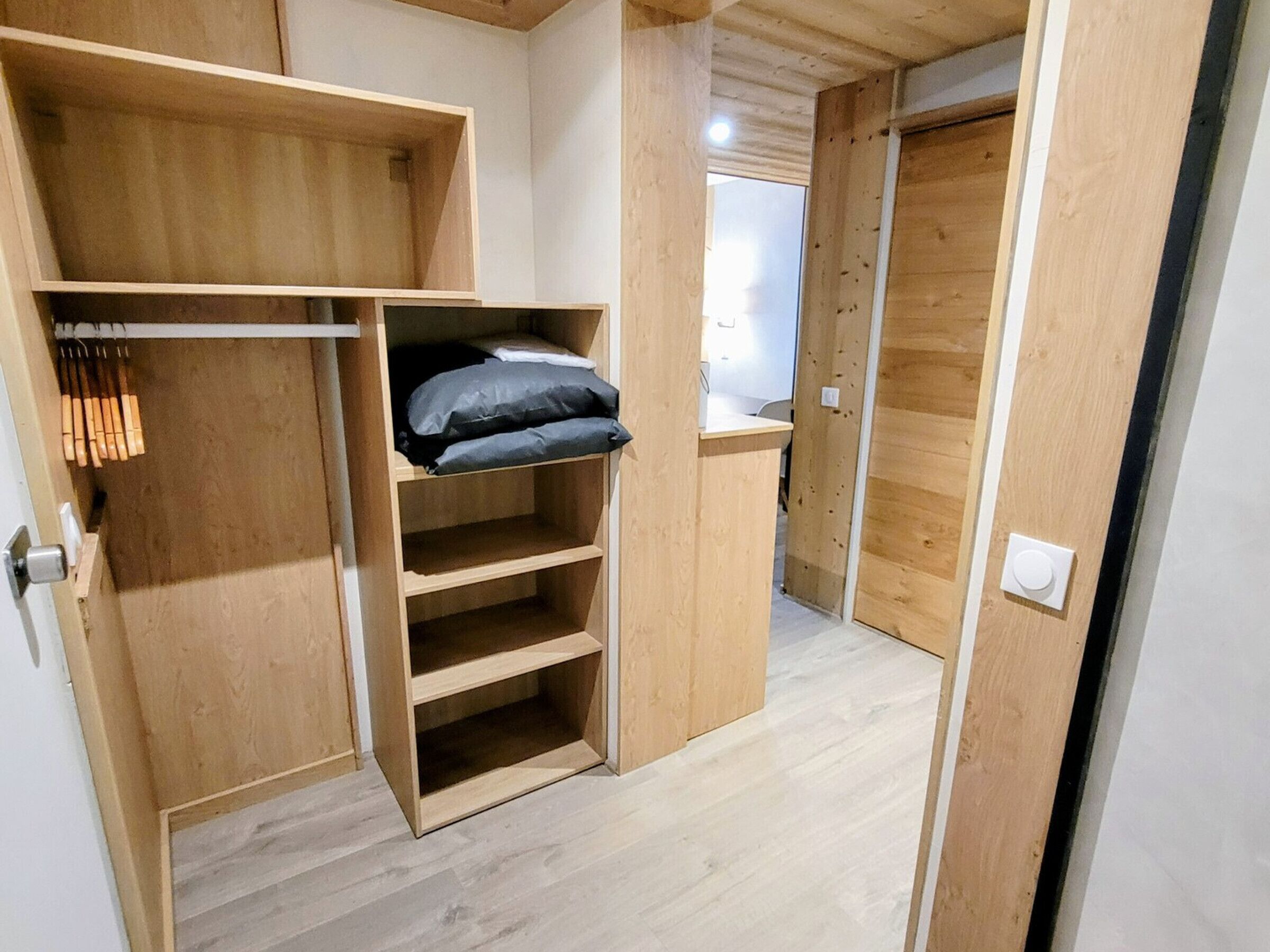 A compact room with built-in wooden shelving, a bed with pillows, and a door leading to another room.