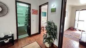 A hallway with a wooden floor, a potted plant, a mirror, and a painting on the wall. - A Casa de Sesimbra com VISTA MAR (Sesimbra)