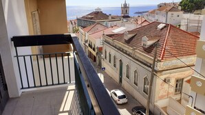 A balcony overlooking a street with buildings, a car, and a clear view of the sea. - A Casa de Sesimbra com VISTA MAR (Sesimbra)