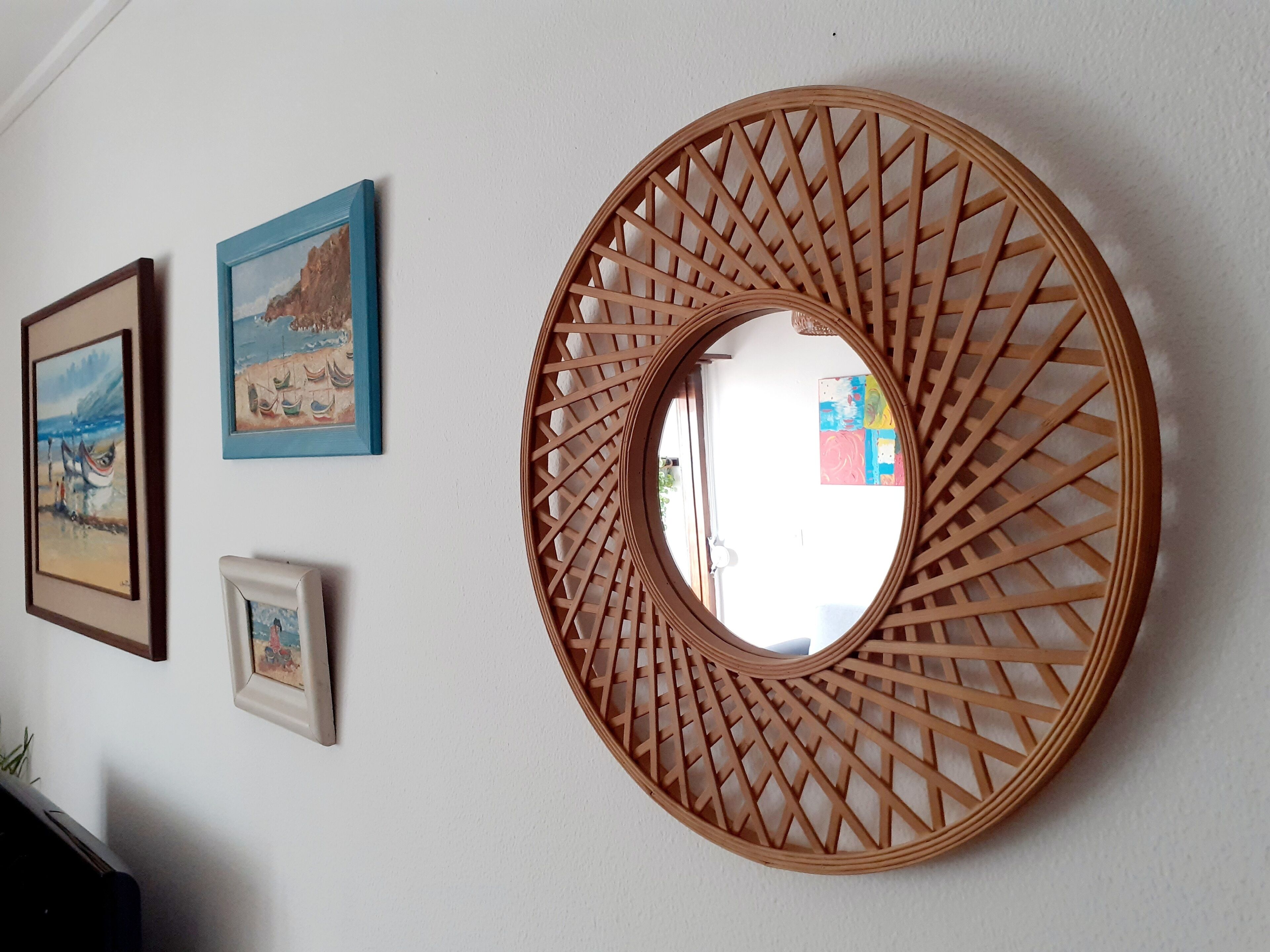 A wall with three framed artworks and a large circular mirror with a lattice design.