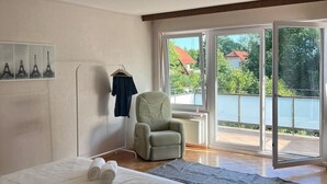 Ein Schlafzimmer mit Bett, Sessel und Seeblick durch eine Schiebetür.