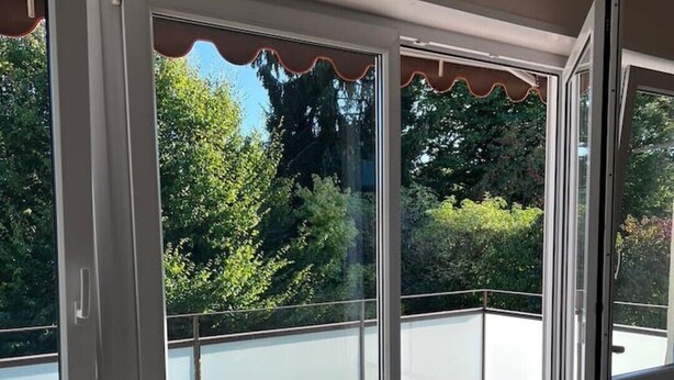 Ein Zimmer mit einer Schiebeglasdoor zum Balkon mit Blick auf Grünflächen und ein Gewässer.
