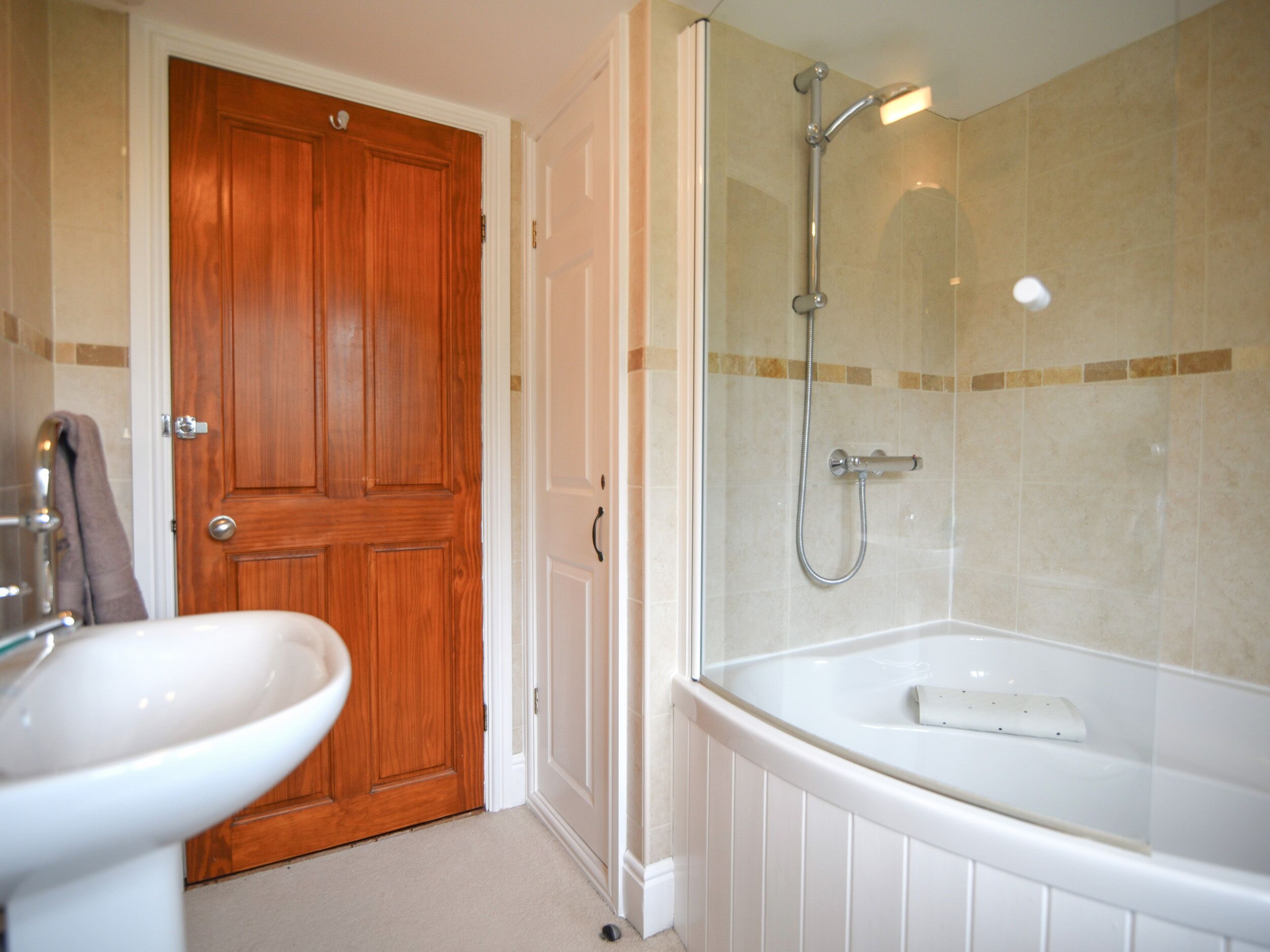 Une salle de bain avec une porte en bois, un lavabo blanc et une baignoire équipée d’un pommeau de douche.