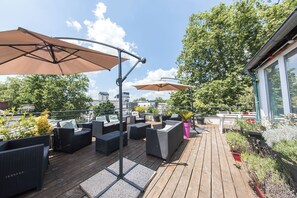 A rooftop patio with outdoor furniture, umbrellas, and potted plants.