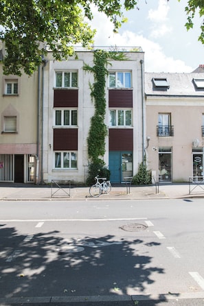 A building with a bicycle parked in front, a blue door, and a visible window.