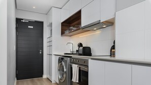 A compact kitchen with a washing machine, oven, and a coffee maker on the countertop. - 16 on Bree 1419 (Cape Town)