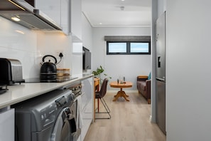 A compact kitchen with a washing machine, a kettle, and a microwave. There is a dining area with a table and chairs, and a sofa.