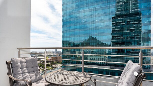 A balcony with two upholstered chairs and a small round table, overlooking a modern glass building. - 16 on Bree 1419 (Cape Town)