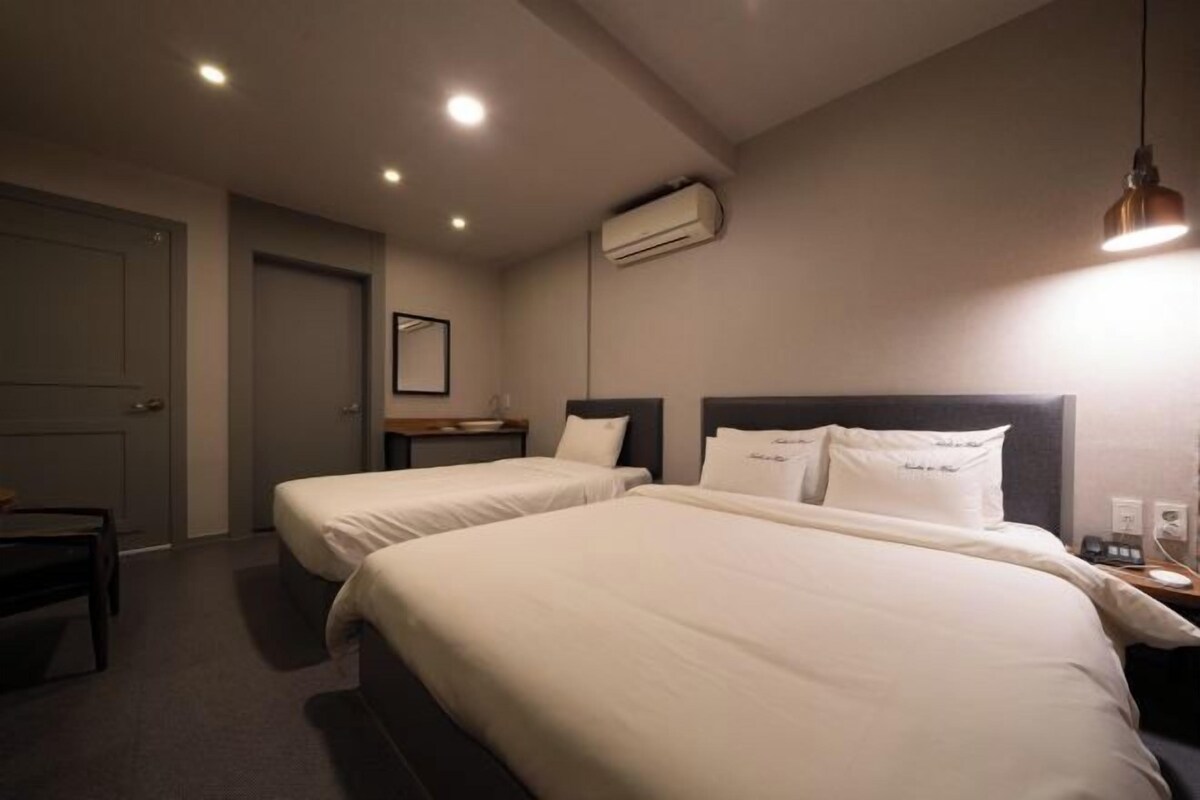 Camera d'albergo con due letti, una scrivania, una sedia, un condizionatore d'aria e una lampada a sospensione.