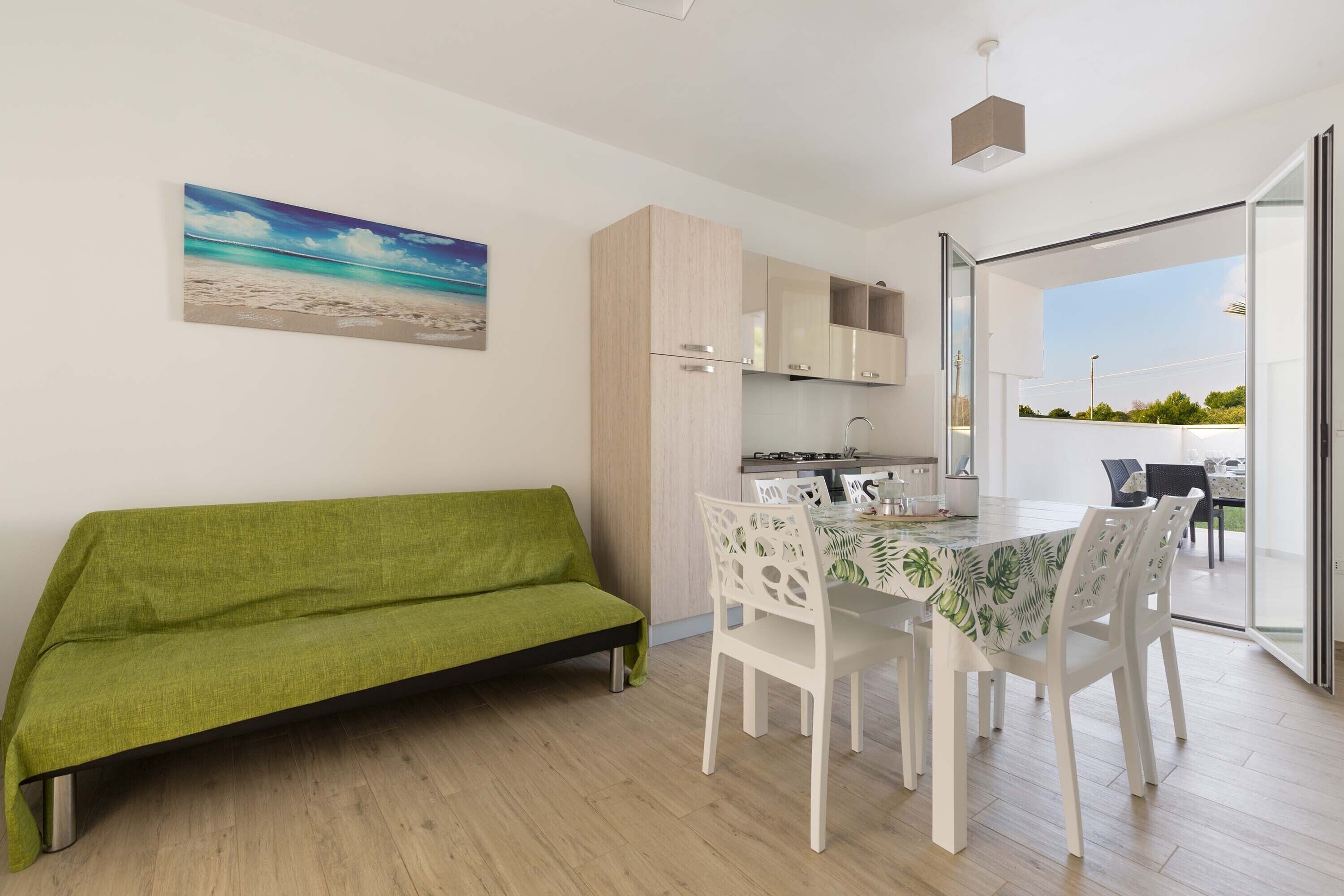 Eine moderne Küche mit weißen Schränken, einem Esstisch mit weißen Stühlen und einem grünen Sofa.