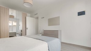 Une chambre moderne avec un grand lit, une armoire, une table de chevet et un miroir.
