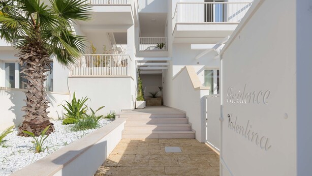 Un bâtiment moderne à la façade blanche, avec un palmier et un escalier menant à un niveau supérieur.