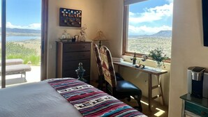 A bedroom with a bed, a desk, a chair, a dresser, and a view of a landscape through large windows.