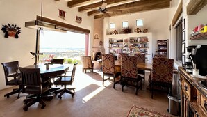 A spacious dining area with a high ceiling and exposed beams, a fireplace, and a bookshelf filled with books and decorative items.
