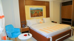 A hotel room with a bed, a blue chair, a small table with a remote control, and a painting on the wall. - Abat Guest House (Addis Ababa)