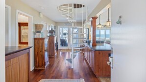 A kitchen with wooden cabinets, a built-in island, and a spiral staircase leading to an upper level. - Oceanfront Condo in WILD DUNES! Fully Renovated with Rooftop Balcony! (Isle Of Palms)