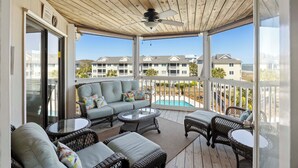 A covered outdoor area with wicker furniture, a ceiling fan, and a view of a swimming pool and buildings in the background. - Oceanfront Condo in WILD DUNES! Fully Renovated with Rooftop Balcony! (Isle Of Palms)