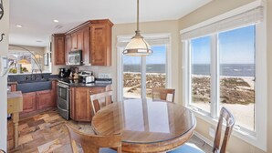 A kitchen with wooden cabinets, a stainless steel stove, and a dining table with chairs. - Oceanfront Condo in WILD DUNES! Fully Renovated with Rooftop Balcony! (Isle Of Palms)