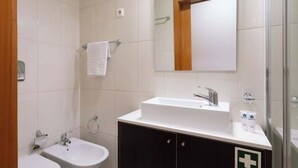Une salle de bain moderne avec un lavabo blanc, un miroir et un meuble noir orné d’une croix médicale.