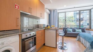 Une cuisine moderne dotée de plans de travail en granit, d’un four encastré et d’un lave-vaisselle. On y trouve un petit coin repas avec un tabouret de bar et un canapé. De grandes fenêtres offrent une vue sur l’extérieur.