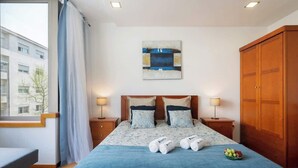 Une chambre d’hôtel comprenant un lit, deux tables de chevet, une armoire, une fenêtre avec des rideaux et un tableau accroché au mur.