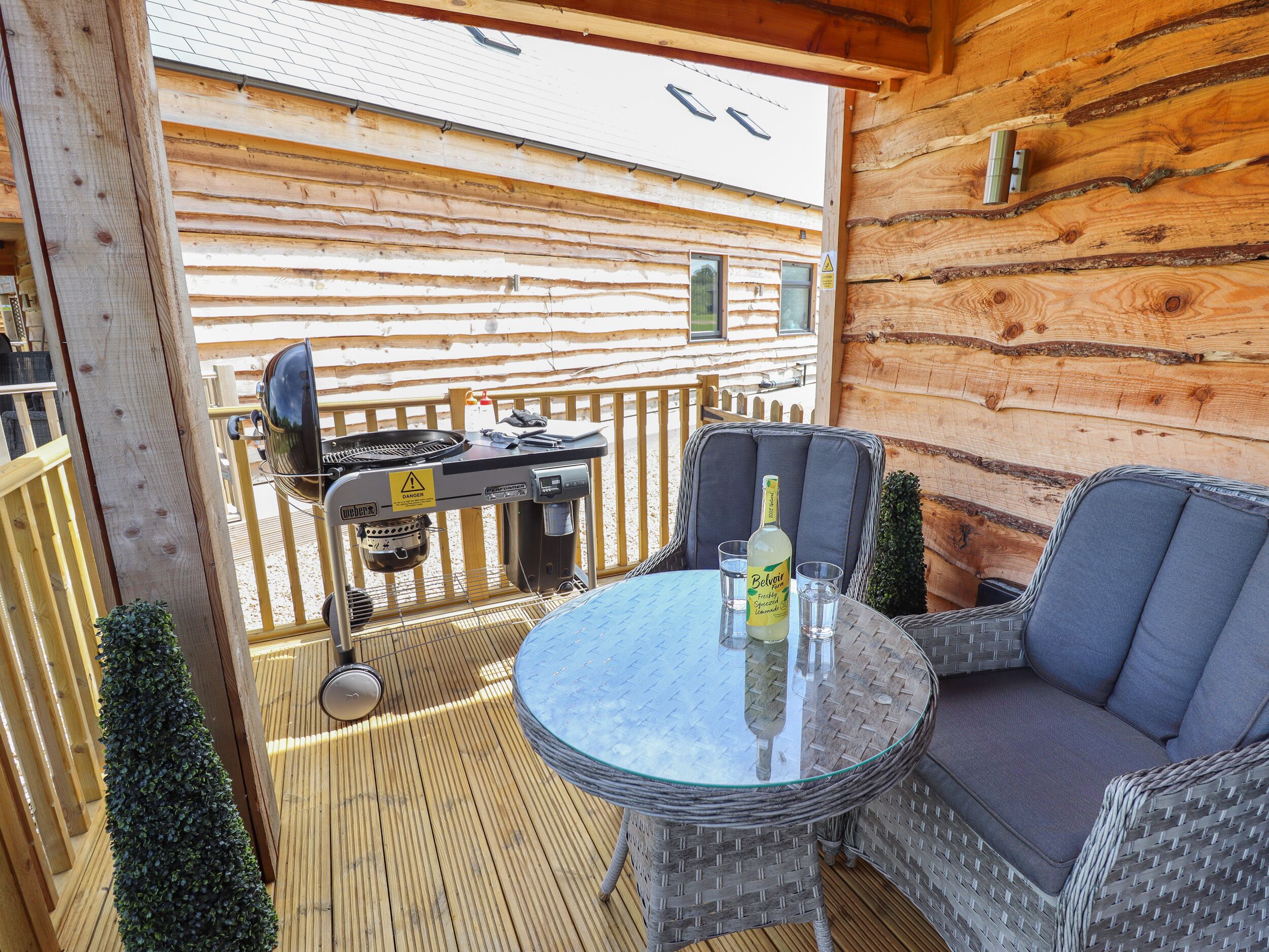 Een houten terras met een barbecue, een tafel met een fles en twee stoelen.
