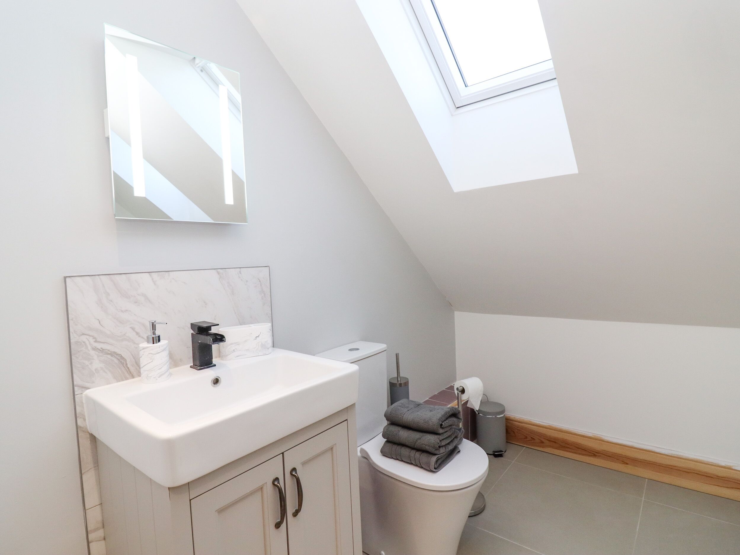 A modern bathroom with a skylight, a white sink, a toilet, and a mirror above the sink.